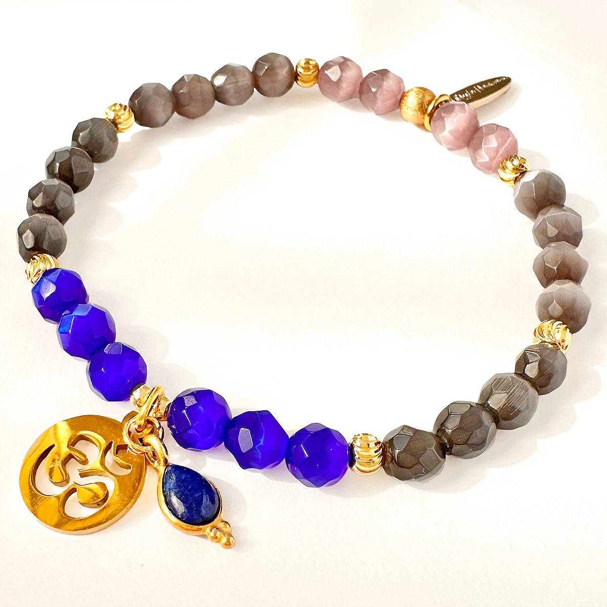 Serenity Om Armband aus Katzenauge-Quarz mit blauem Akzent und goldenem Om-Anhänger.